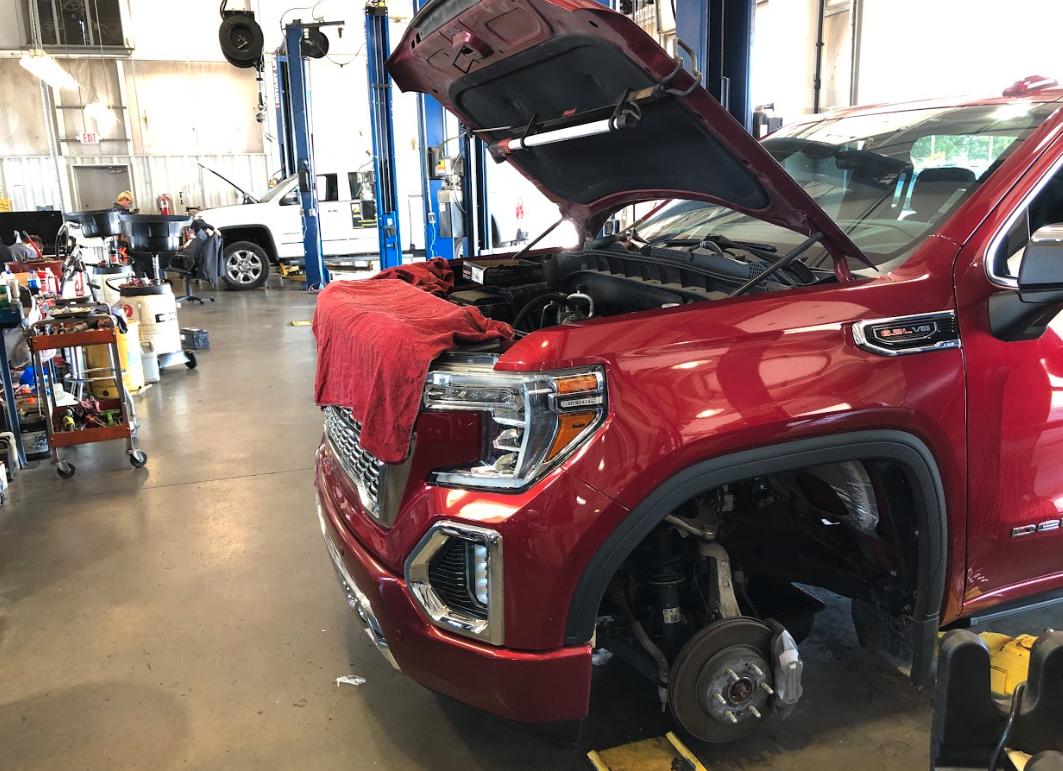 Red GMC truck undergoing service at Crain Buick GMC in Springdale with hood open and tire removed